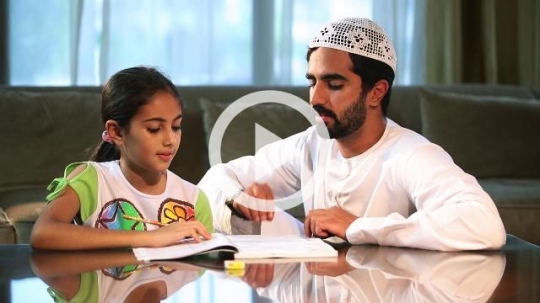 Arab man sitting next to his daughter working on her homework |