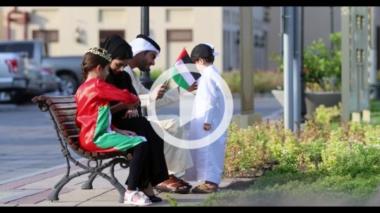 Middle Eastern family sitting on the bench preparing for the celebrations of the UAE National Day|