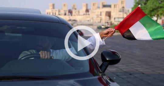 Arab man waving the UAE flag outside of his car
