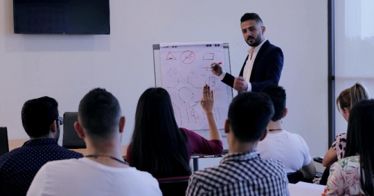Woman raises her hand in the classroom to ask the professor a question  |-