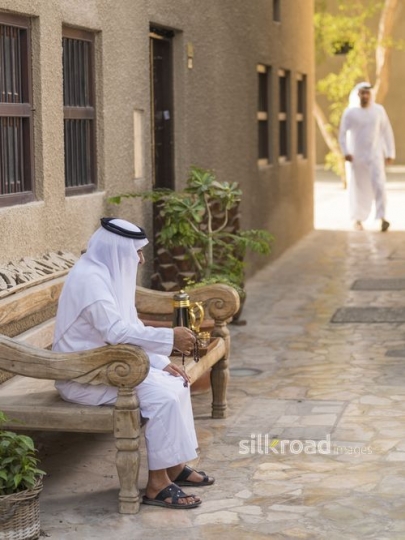 Middle Eastern grandfather sitting with his misbahah while the man is walking towards him|-