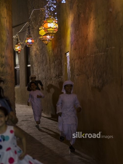 Arab kids running through an alleyway decorated by Ramadan lanterns