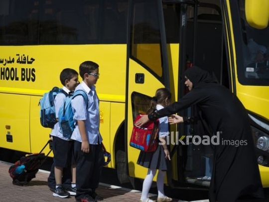 Supervisor helping the young kids on the bus|-