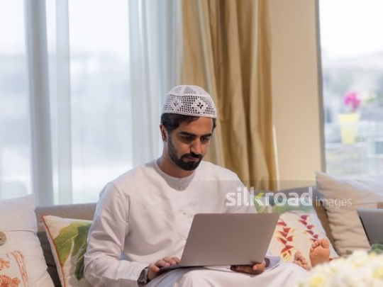 Middle Eastern man sitting on the couch using the device |