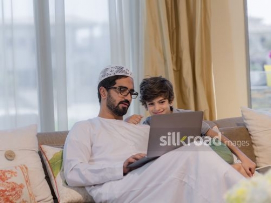 Middle Eastern man and boy using the device on the couch|