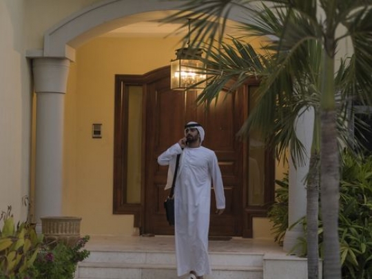 Arab man leaving his house while on the phone|-