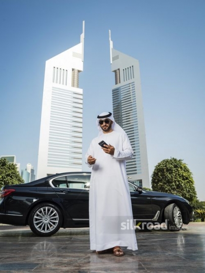 Businessman standing infront of his car wearing his sunglasses using his mobile|-