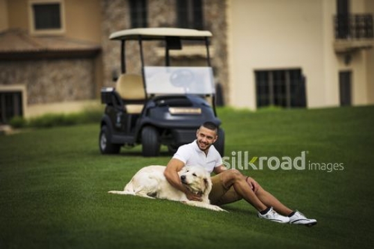 Young Middle Eastern man sitting on the grass next to the dog|-