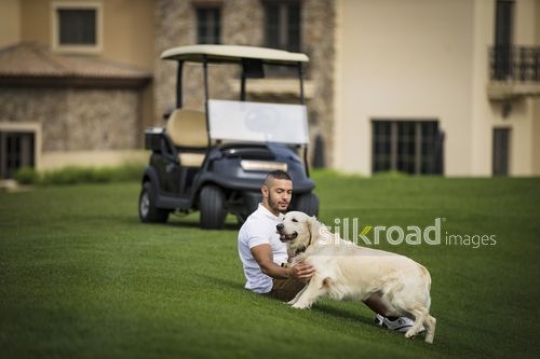 Middle Eastern man sitting on the grass with the dog|-