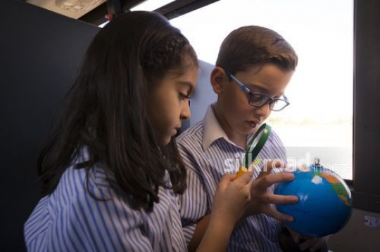 Middle Eastern Kids looking at the globe through the magnifying glass|-