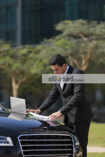 Businessman standing by his car doing work|
