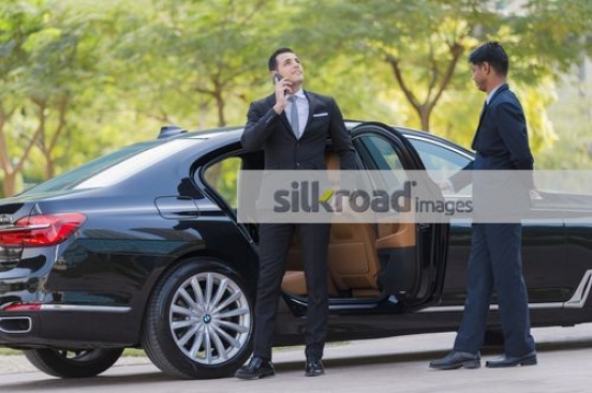 Businessman getting out of the car while talking on the phone|