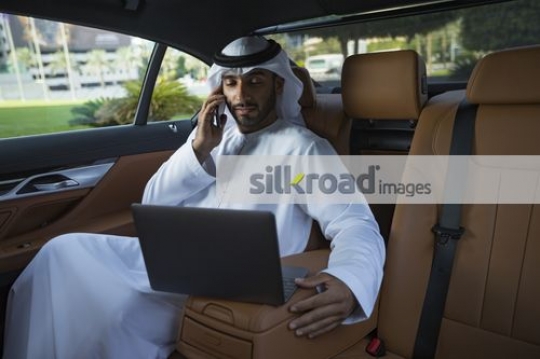 Middle Eastern Businessman sitting inside the luxury car talking on the phone |