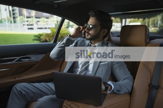 Businessman sitting in the backseat of the car talking on the phone|