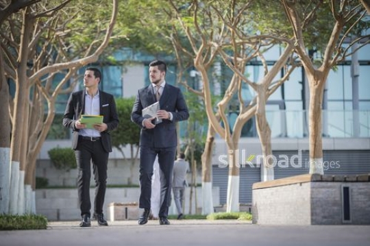 Western Businessman and Middle Eastern Businessman carrying folders walking together|-