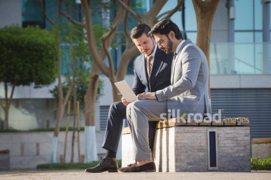 Two employees sitting outside together working from the laptop|-