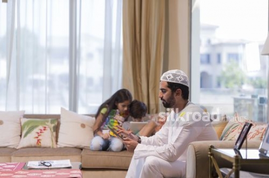 Middle Eastern family sitting together on the couch together using their devices|