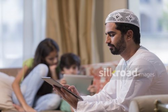 Middle Eastern man on the device with the kids in the back|