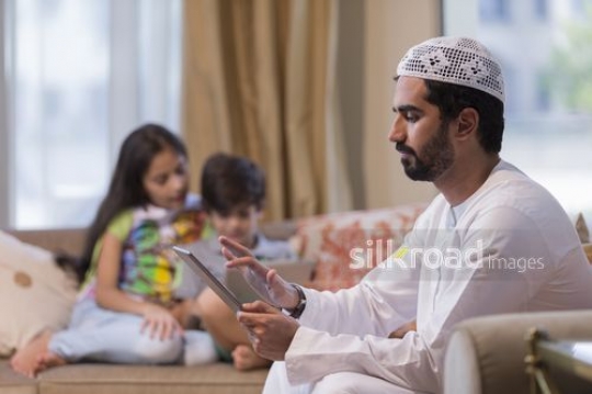 Middle Eastern family sitting on the couch using their devices|