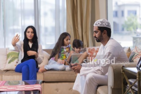 Middle Eastern woman taking a photo of herself sitting with the middle eastern man and young kids|