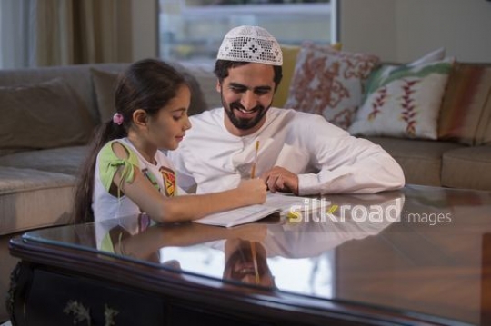 Middle Eastern man helping the young girl with her homework |