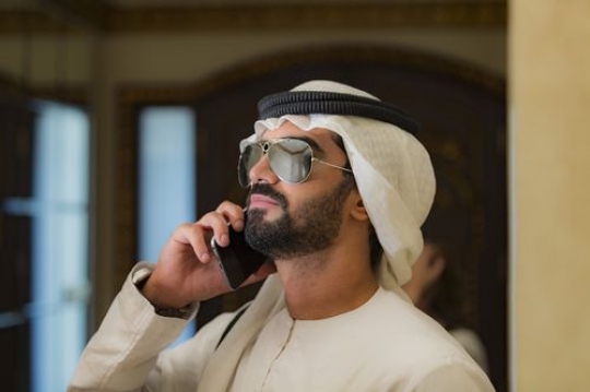 Arab mn dressed in the traditional UAE attire talking on the phone|-