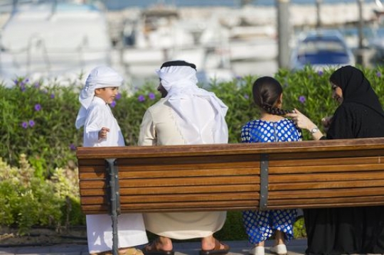 Arab family dressed in traditional attire sitting on the bench|-