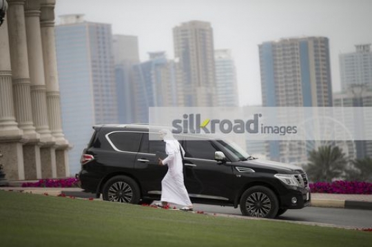 Businessman dressed in the traditional attire walking next to the big car|