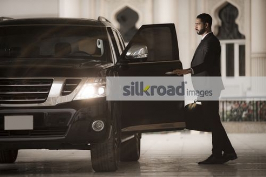 Middle Eastern businessman dressed in suit closing the door of the car|