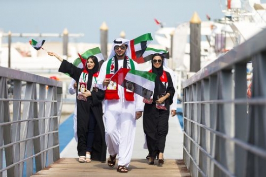 A group of people carrying UAE flags during a National Day parade|
