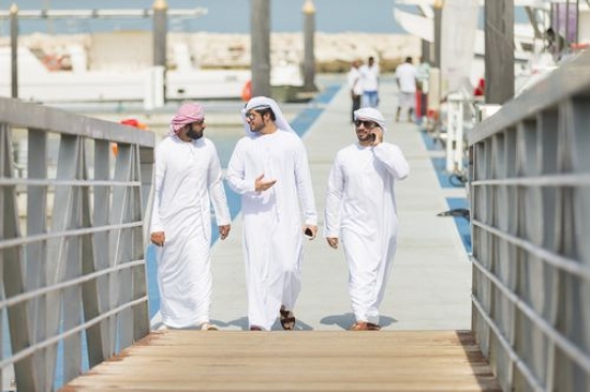 Two men walking towards the dock while one man is talking on the phone|