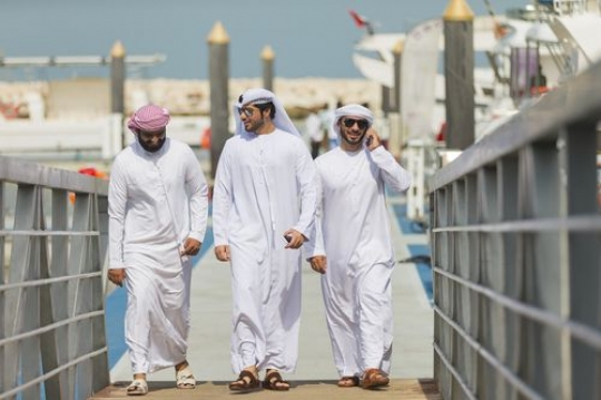 One man talking on the phone while walking with two other men on the dock|