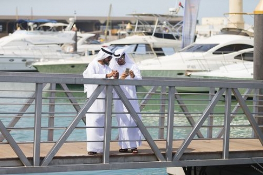 Arab men dressed in the traditional UAE attire standing by the dock talking to each other|