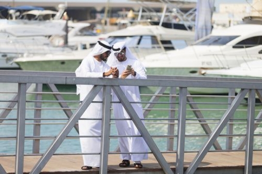 Arabian men dressed in the traditional UAE attire standing by the dock talking to each other|