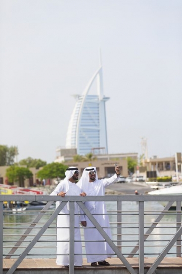 Middle eastern men standing by the dock taking a photograph together with a well-known landmark behind them|