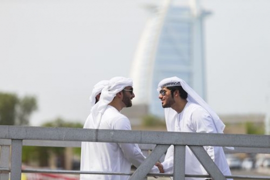 Arab men greeting each other while standing on the dock with a background of a well-known landmark|