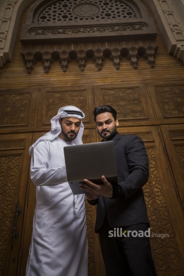 Middle Eastern man standing with his colleague using the laptop|-