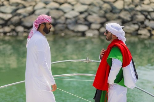 Arab man carrying the UAE flag on his shoulder while talking to his friend|