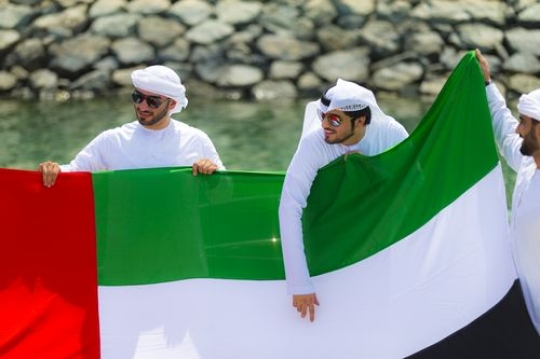 Three arab men holding a UAE Flag during the celebrations of National Day|