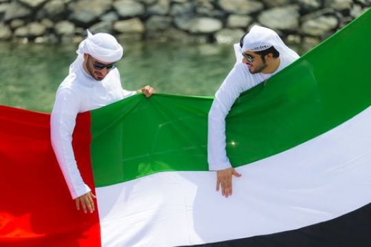 Arab men holding the UAE flag during the celebrations of National Day|
