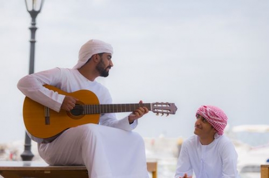 Man playing the instrument while sitting with his friend|