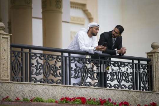 Arab businessmen leaning on the bridge rail talking to each other|-