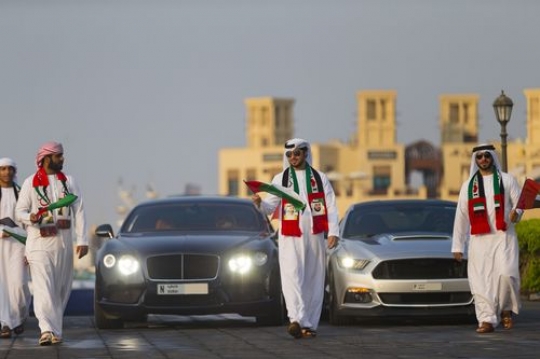 A group of men dressed in the traditional attire followed by luxury cars during a UAE National Day parade|
