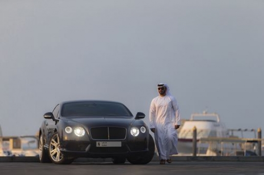 Motion of an arab man dressed in the UAE traditional attire walking away from his vehicle|-