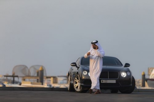 Arab man dressed in traditional attire talking on the phone is walking away from his parked vehicle|-