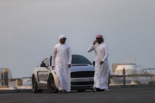 Arab men walking away from parked car, while one man is talking on the phone|-