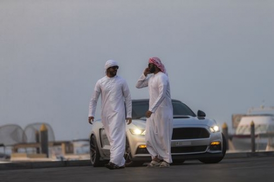 Arab man talking on the phone while him and his friend are walking away from the car|-