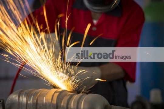Mechanic using machine to cut the metal part for the car at the workshop|