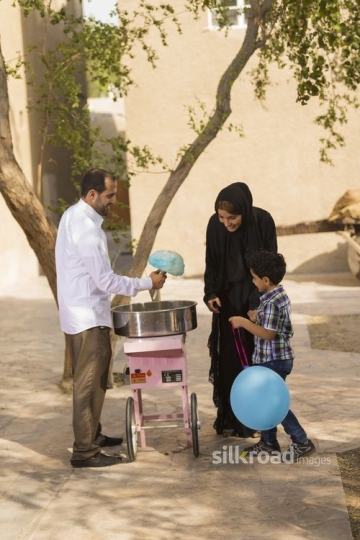 Arab man offering cotton candy to the mother and the kid|-
