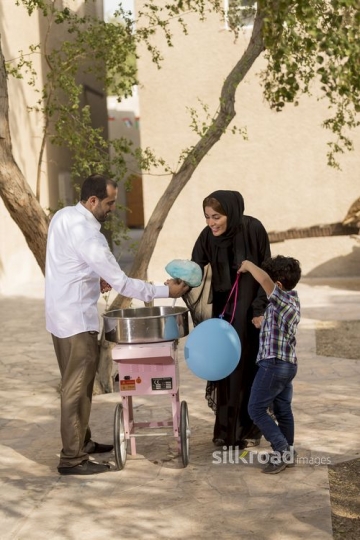 Arab man offering the mother and kid cotton candy|-
